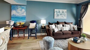 A living room with a brown sofa, a blue armchair, a coffee table, and a painting of horses.