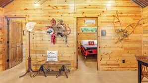 Ein Interieur einer Holzhütte mit einem Bett, einem Tisch mit einem Hut und einem an der Wand befestigten Regal mit Dekoration.