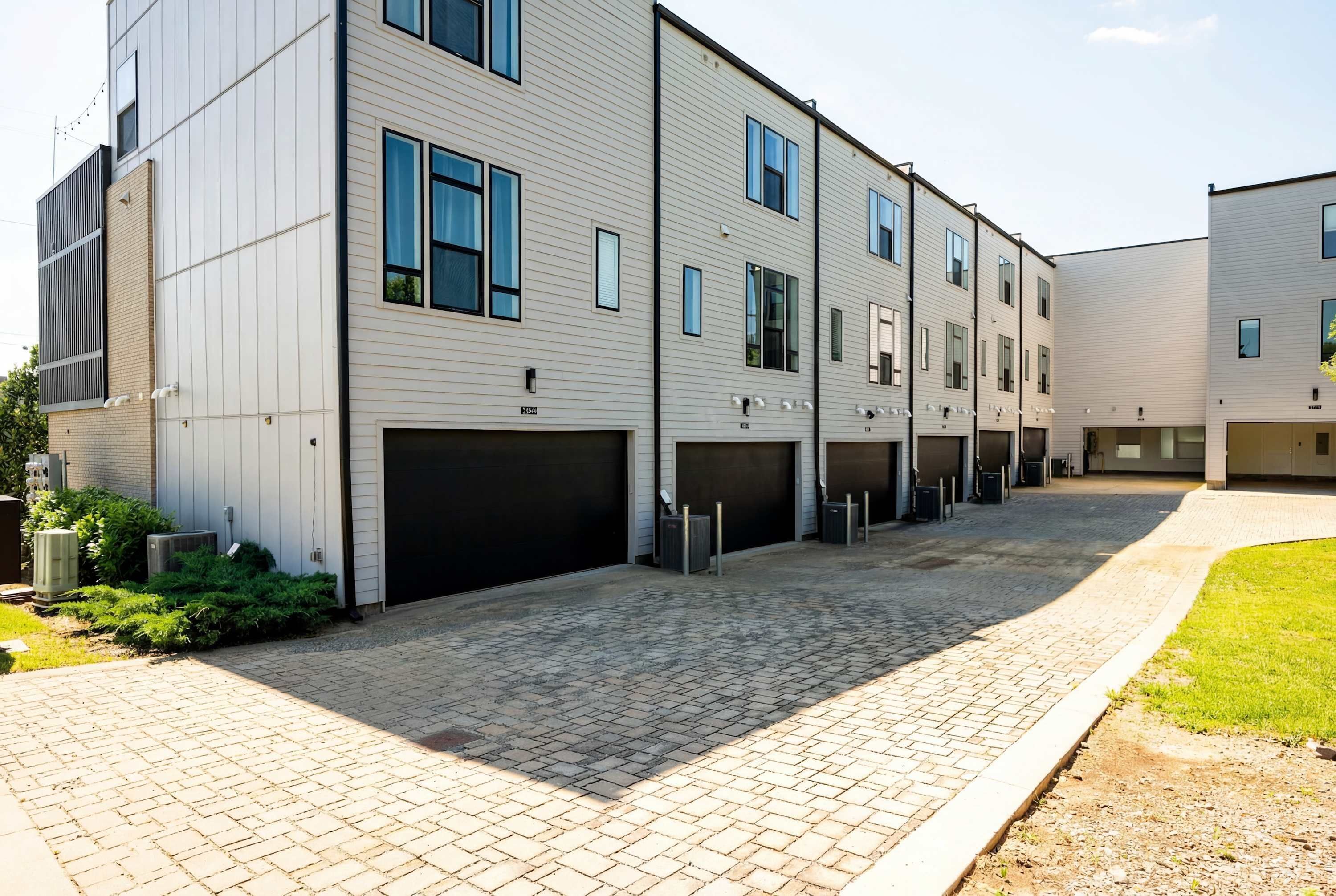 Un bâtiment moderne à plusieurs étages, doté d’une cour pavée de briques, de plusieurs portes de garage et d’une pelouse bien entretenue.