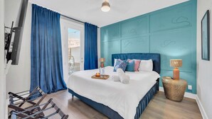 Une chambre avec un grand lit, un téléviseur fixé au mur, un ventilateur de plafond et une vue sur l’extérieur.