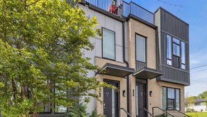 Un immeuble résidentiel moderne à plusieurs étages, doté d’une façade en briques, de grandes fenêtres et d’un petit jardin à l’avant.