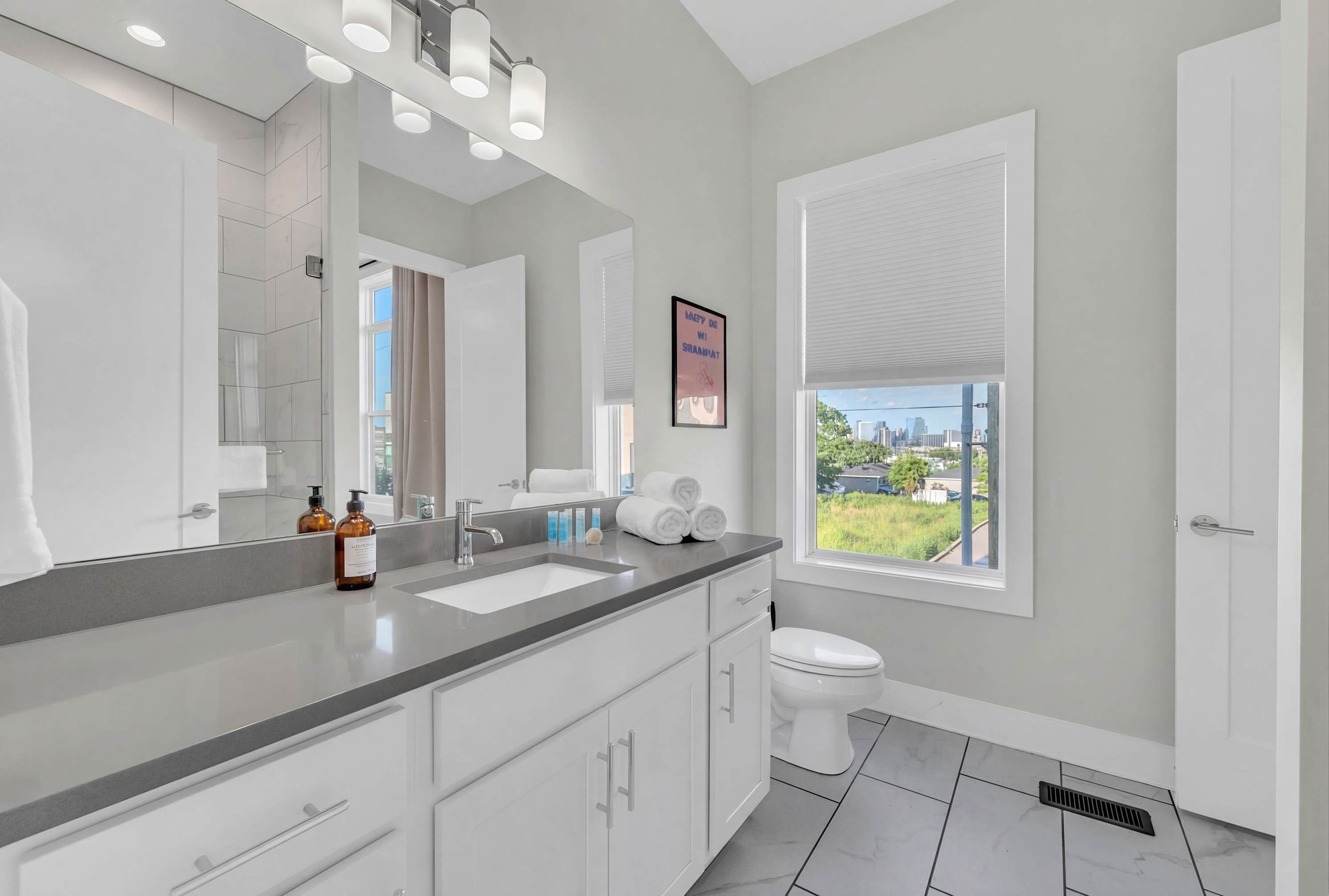 A modern bathroom with a large mirror, a sink, a toilet, and a window with a view.