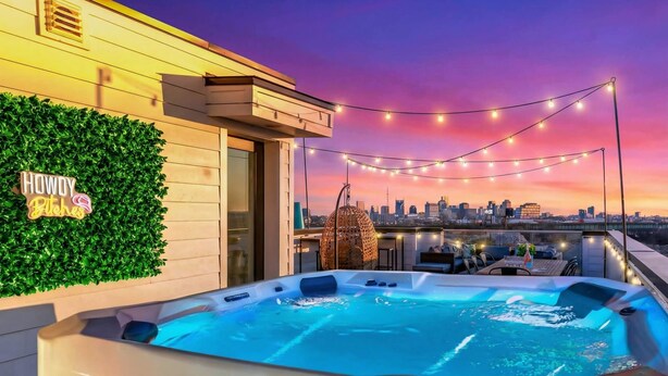 Une terrasse sur le toit avec un jacuzzi, des guirlandes lumineuses, une vue sur les toits de la ville et une pancarte sur laquelle on peut lire : « Salut, les amis ! »