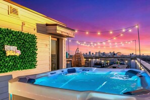 Una terraza con jacuzzi, luces colgantes, vistas al horizonte urbano y un letrero que dice 'HOWDY Pitches'.