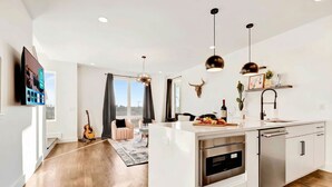 Une cuisine moderne dotée d’un îlot central, d’appareils électroménagers en acier inoxydable, de luminaires suspendus et d’une grande fenêtre.