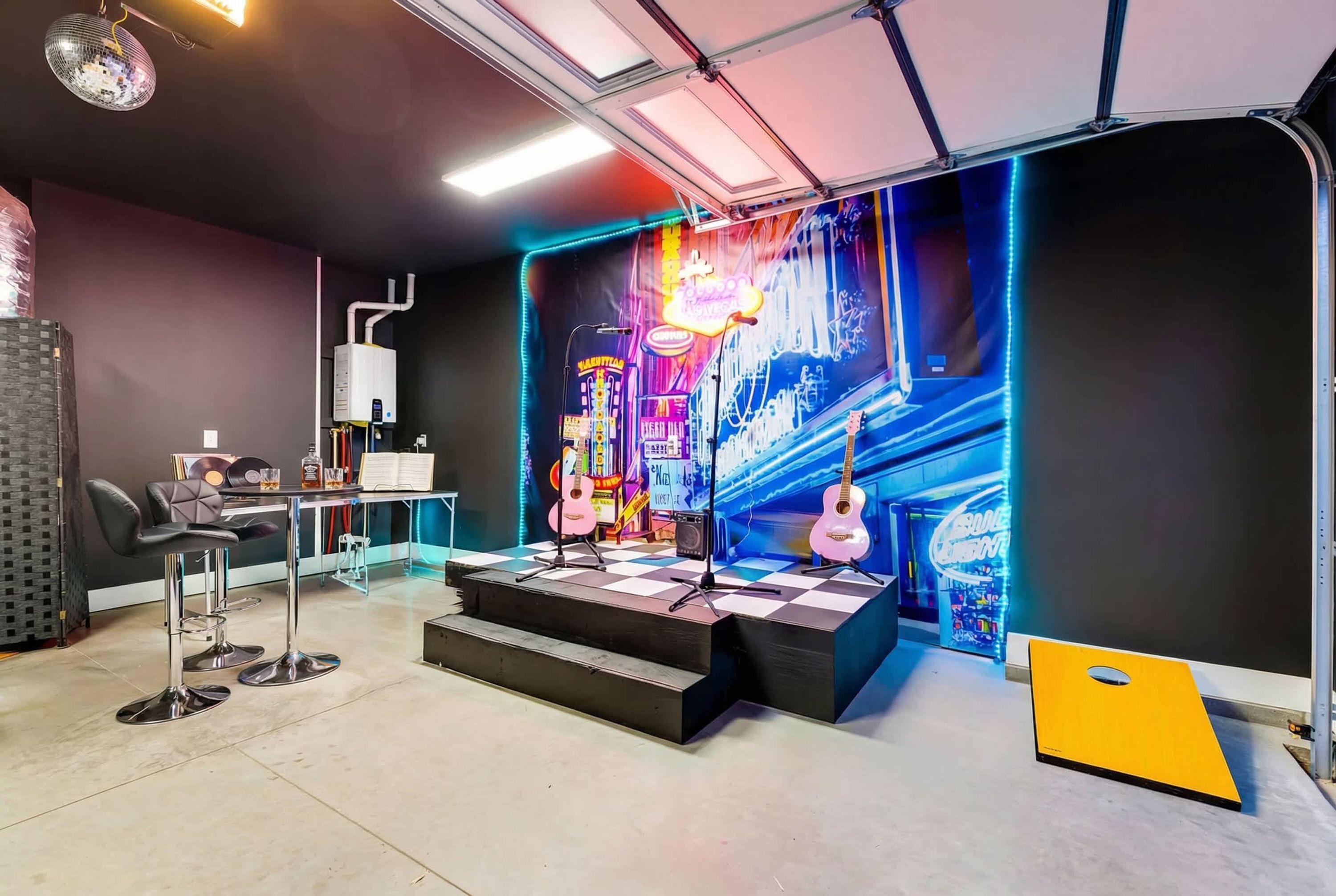 A room with a stage, two guitars, a disco ball, and a neon sign.