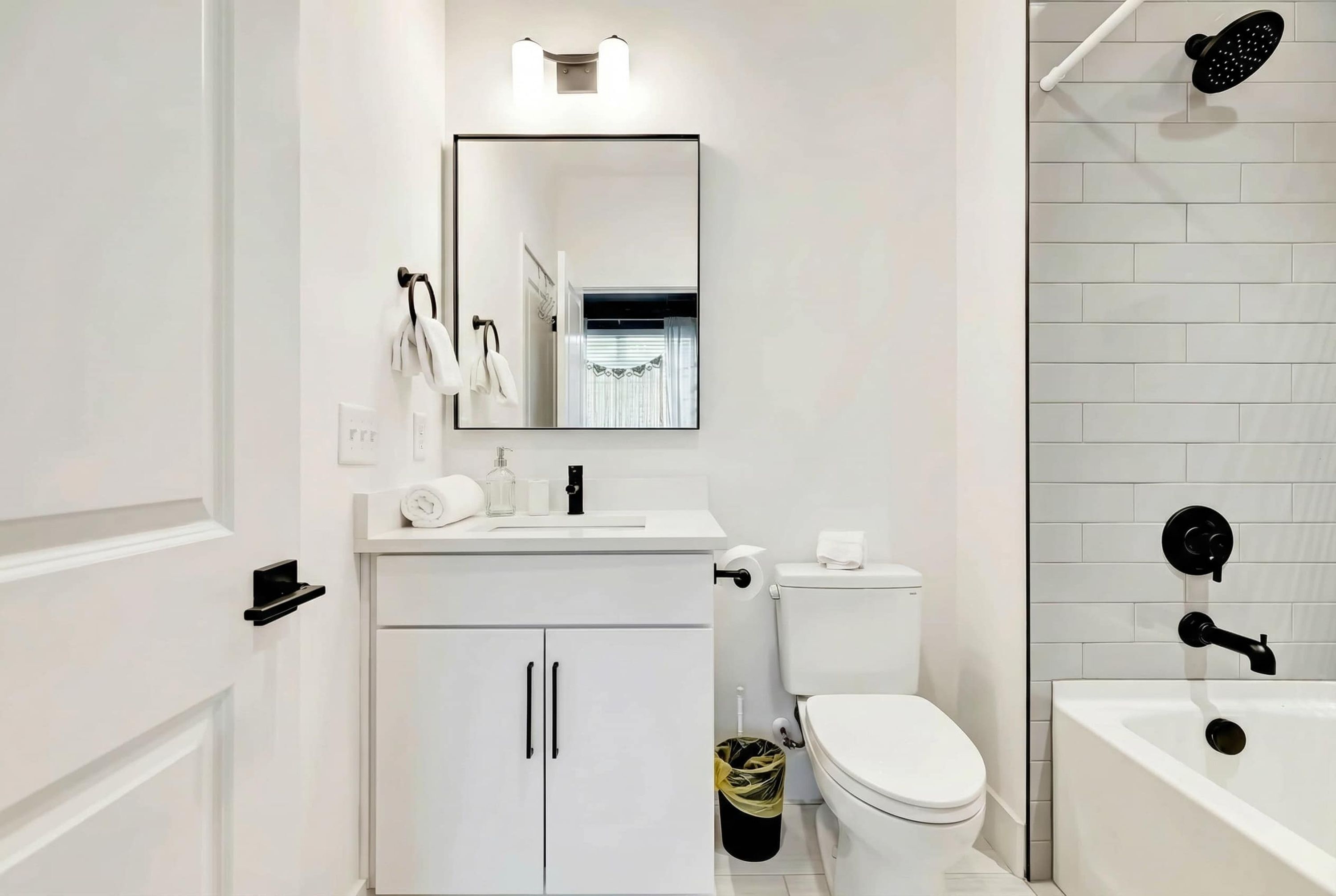 A modern bathroom with a white sink, toilet, and bathtub, a mirror above the sink, and a showerhead on the wall.