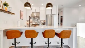 Une cuisine moderne avec des meubles blancs, un réfrigérateur en acier inoxydable et un îlot central doté de tabourets de bar.