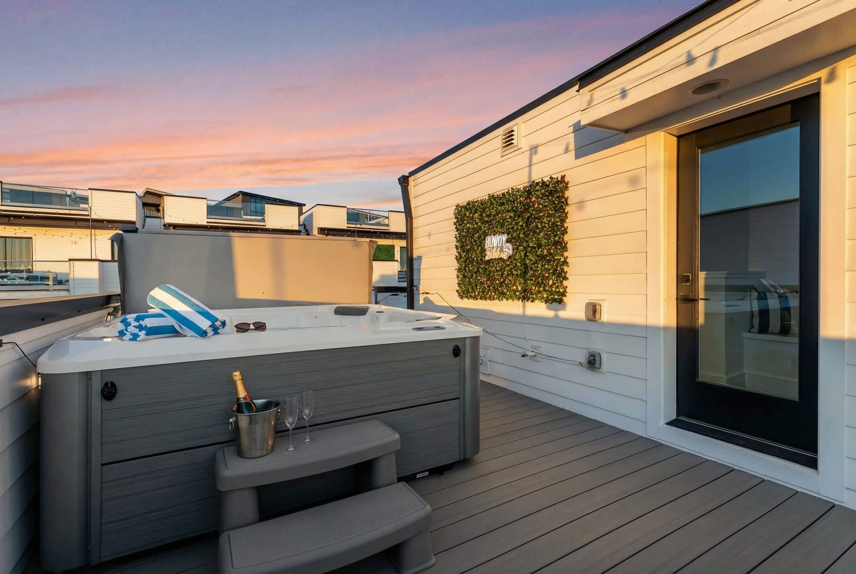 Eine Dachterrasse mit Whirlpool, Champagnerkübel und Gläsern, umgeben von weißen Wänden und einer Glastür.
