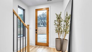 Un intérieur moderne avec un escalier en bois, une grande porte en bois et deux grands plants en pot.