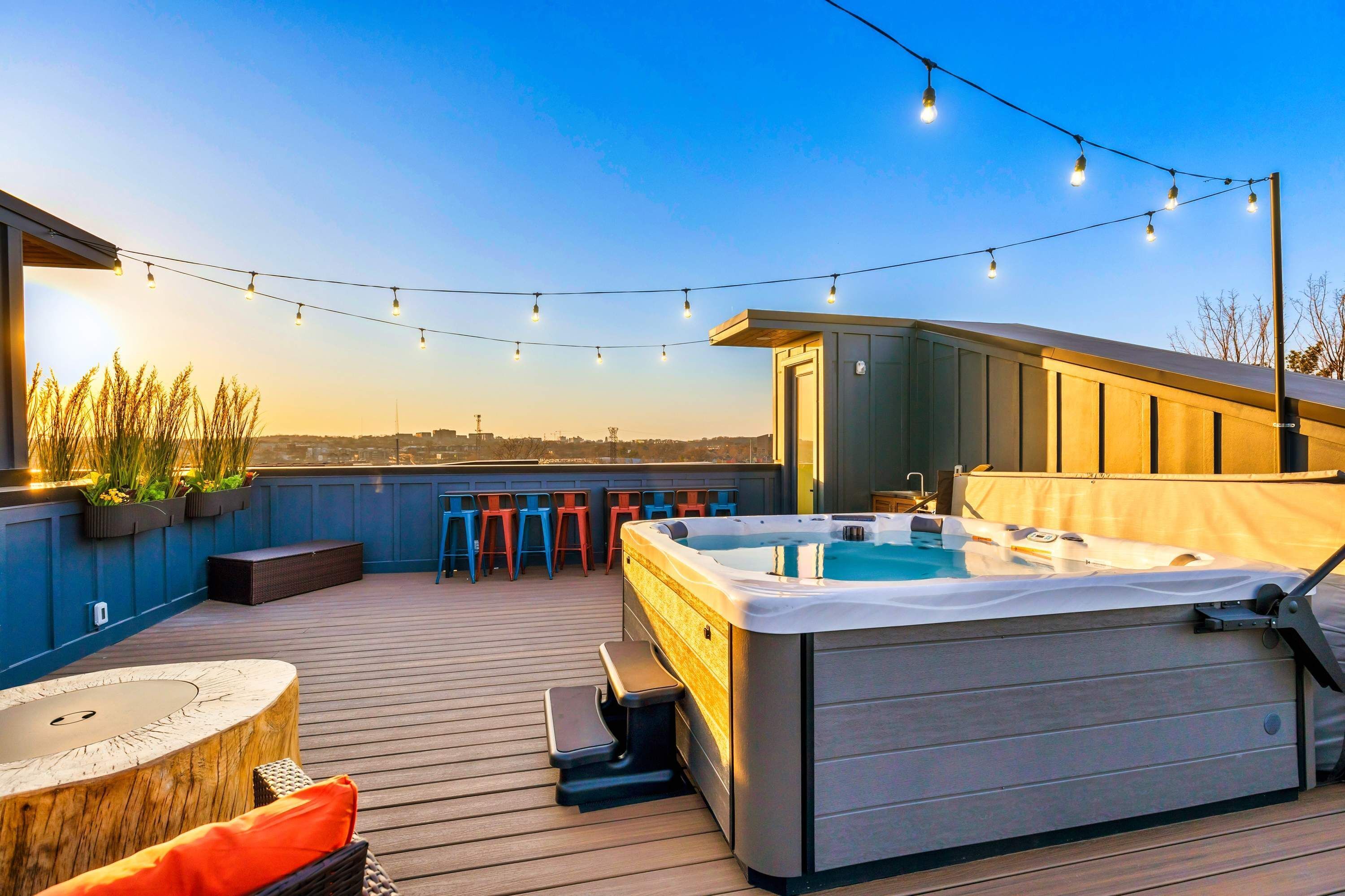 Una terraza en la azotea con un jacuzzi, luces colgantes, asientos exteriores y vistas del horizonte de la ciudad.