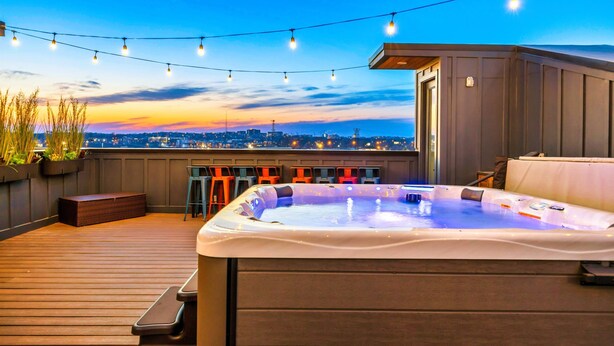 Une terrasse sur le toit avec un jacuzzi, des guirlandes lumineuses et une vue sur la ville au crépuscule.