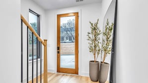 Un pasillo moderno con una escalera de madera, una puerta grande de madera y dos plantas en macetas grandes.