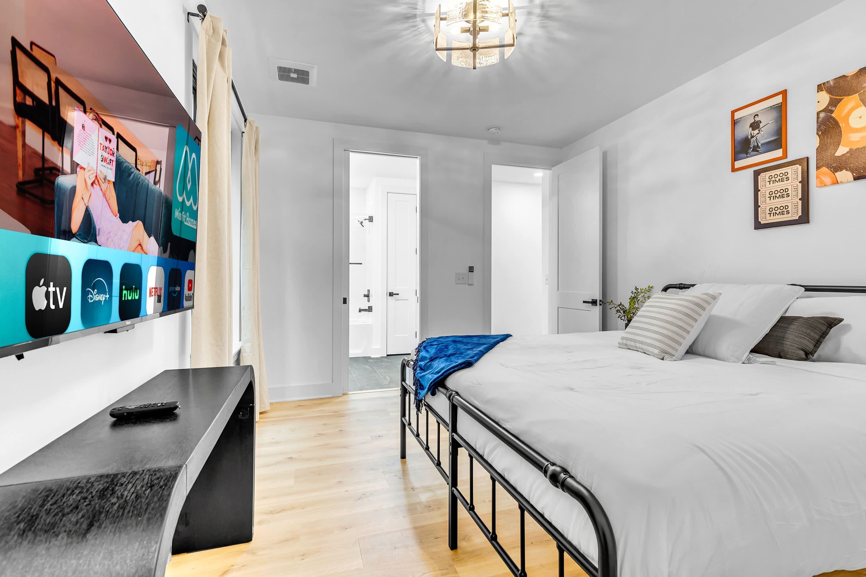 A modern hotel room with a bed, a TV mounted on the wall, and a desk with a remote control.