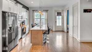 A modern kitchen with stainless steel appliances, a central island with bar stools, and a view of the adjacent dining area. - Rooftop Large Backyard Fire Pit Near Downtown Nashville (Nashville)