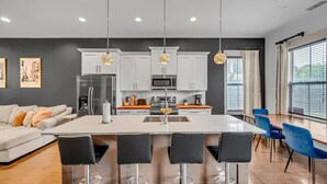 A modern kitchen with white cabinets, a central island with bar stools, and pendant lighting. - Rooftop Large Backyard Fire Pit Near Downtown Nashville (Nashville)