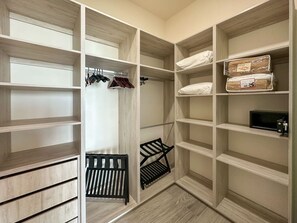 Um closet espaçoso com prateleiras abertas, cabideiro e um banco.