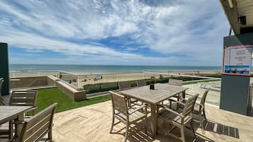 Una terraza con vista a la playa, mobiliario exterior y un letrero.