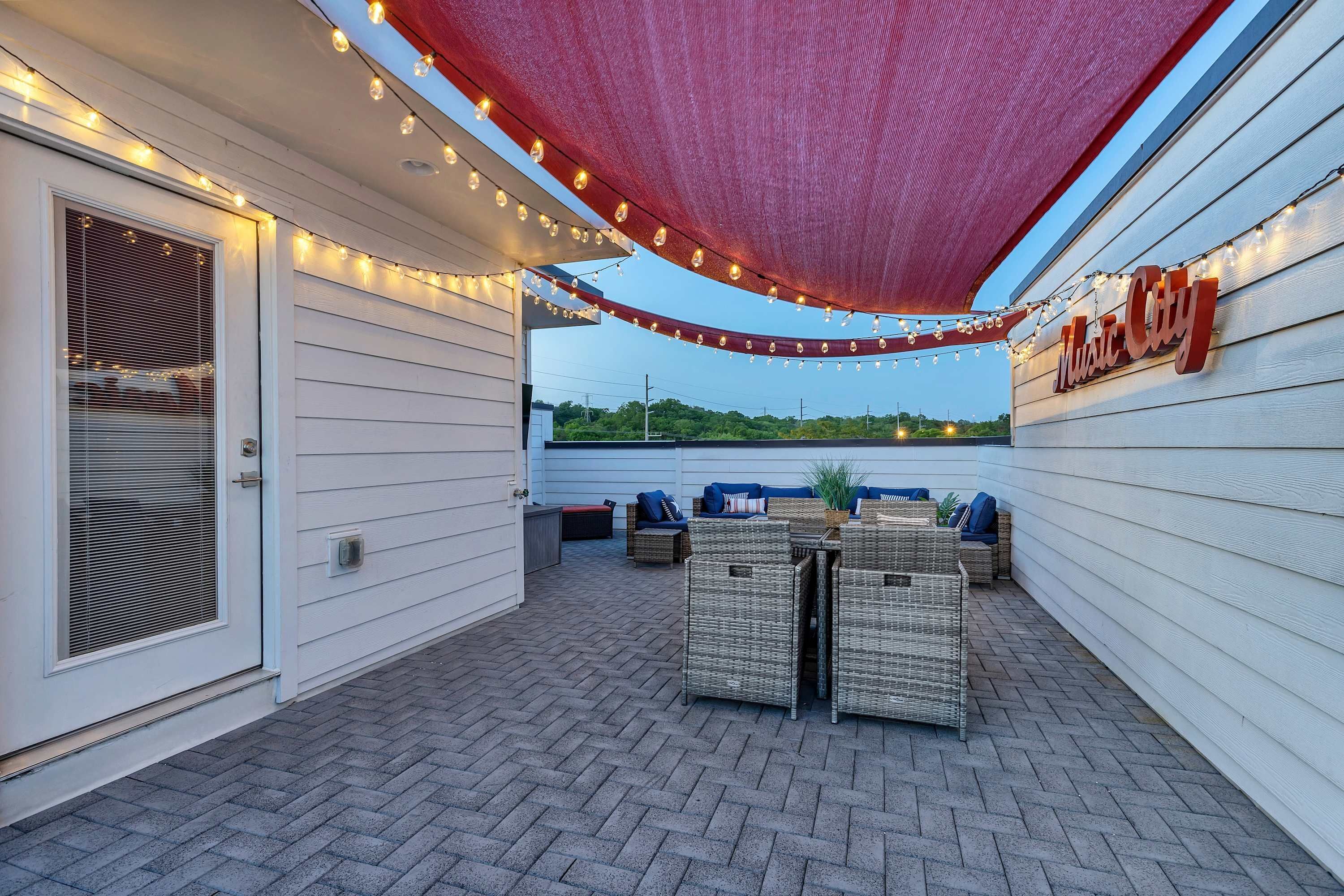 An outdoor patio with wicker furniture, string lights, and a red canopy.