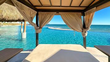 Una habitación frente a la playa con una cama, dos mesas y vistas al océano.