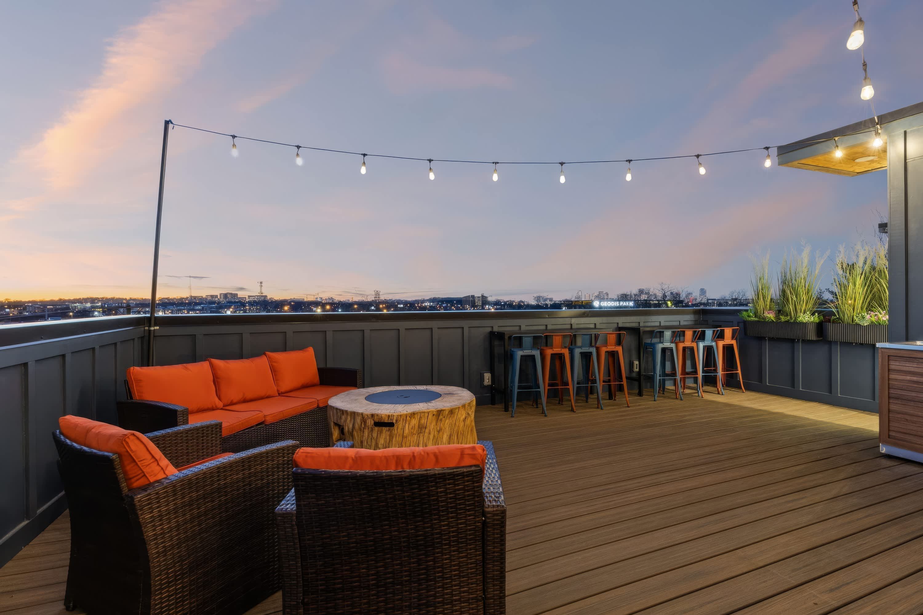 A rooftop terrace with wicker furniture, a bar area, and string lights.