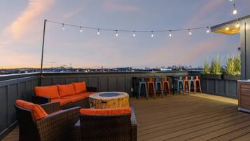 A rooftop terrace with wicker furniture, a bar area, and string lights.