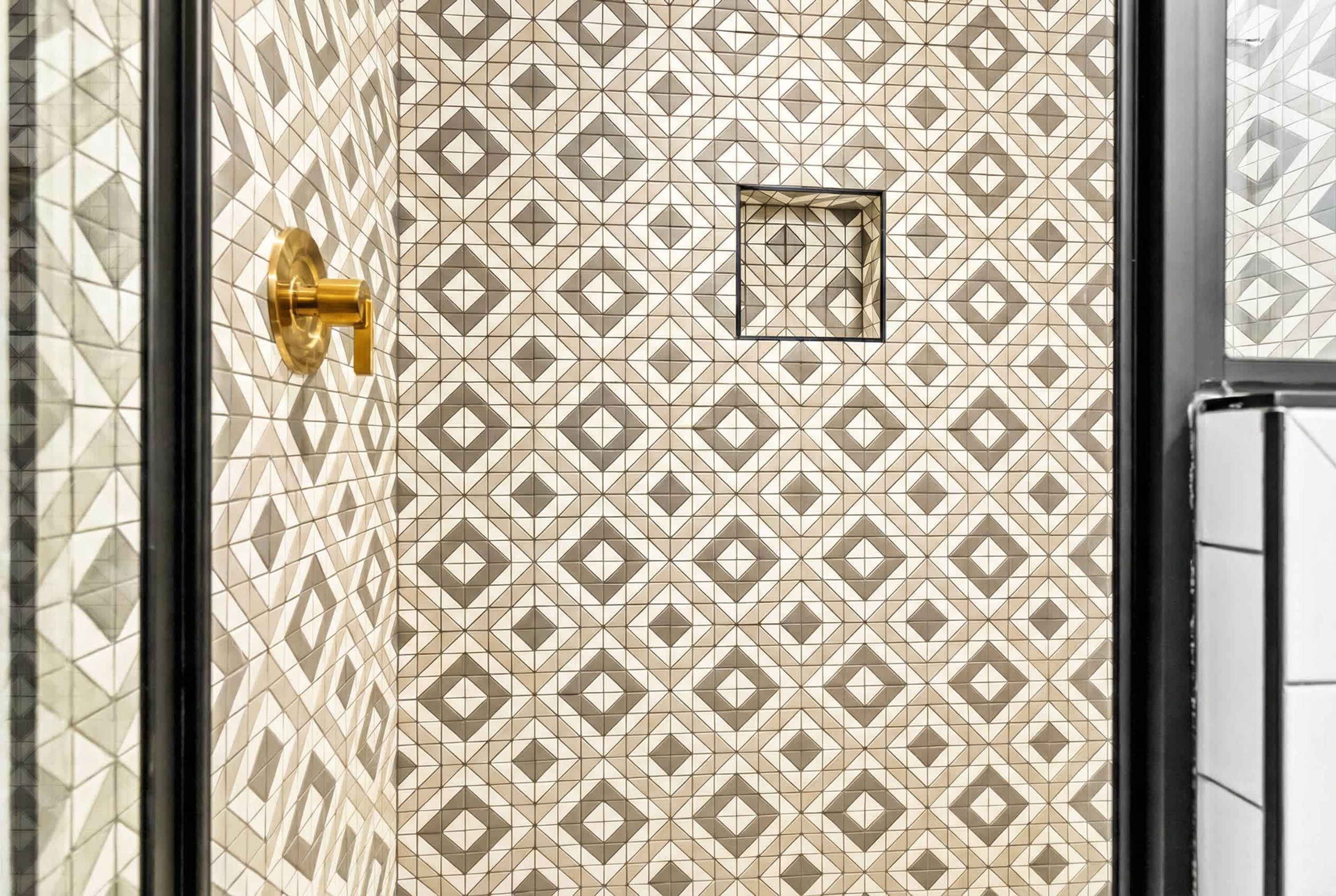 A tiled wall with a geometric pattern, a gold door handle, and a small square window.