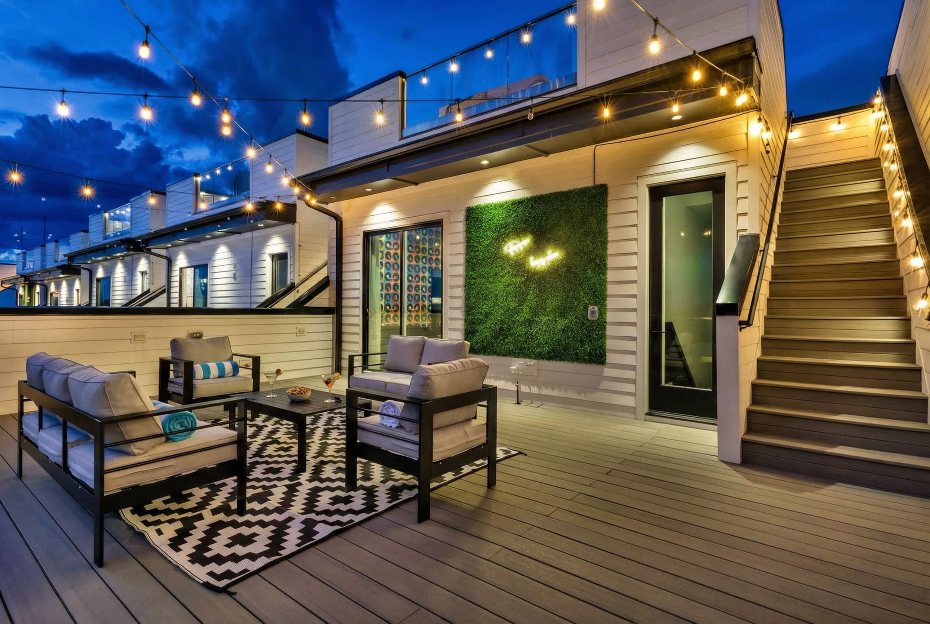 A deck with outdoor furniture, a patterned rug, and string lights.