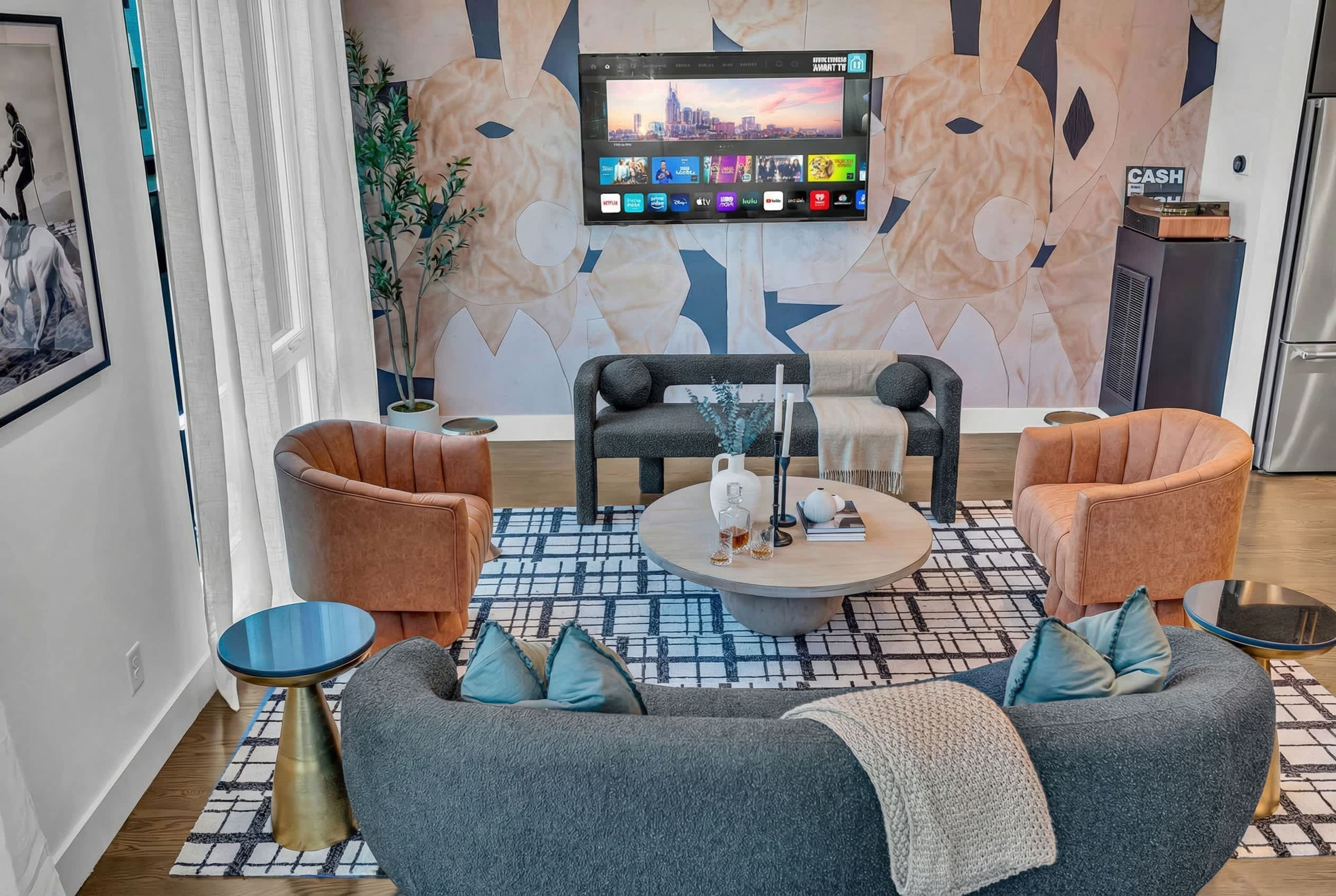 Ein modernes Wohnzimmer mit einer Couch, Sesseln, einem Couchtisch und einem an der Wand montierten Fernseher, der verschiedene Kanäle zeigt.