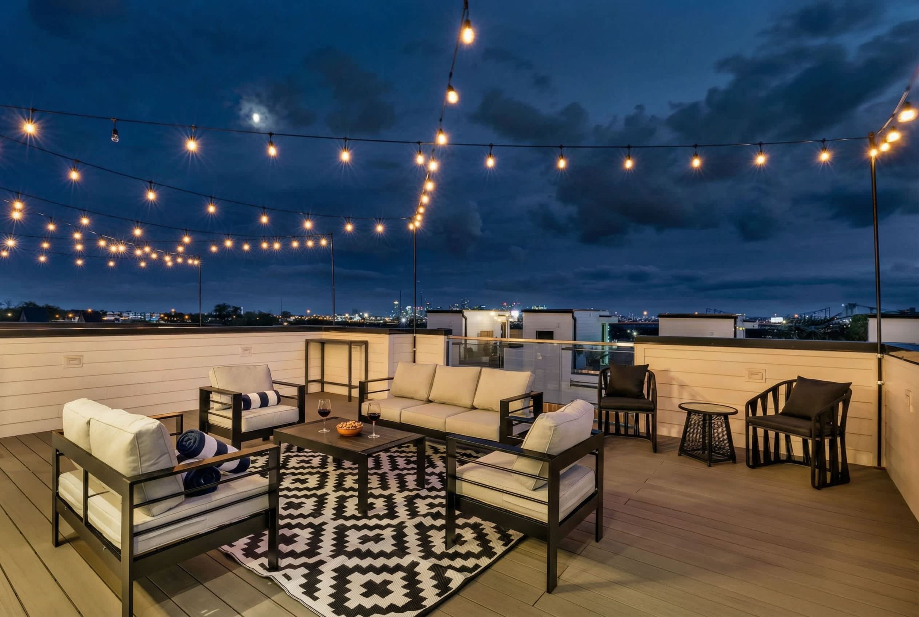 A rooftop terrace with outdoor seating, string lights, and a city view.
