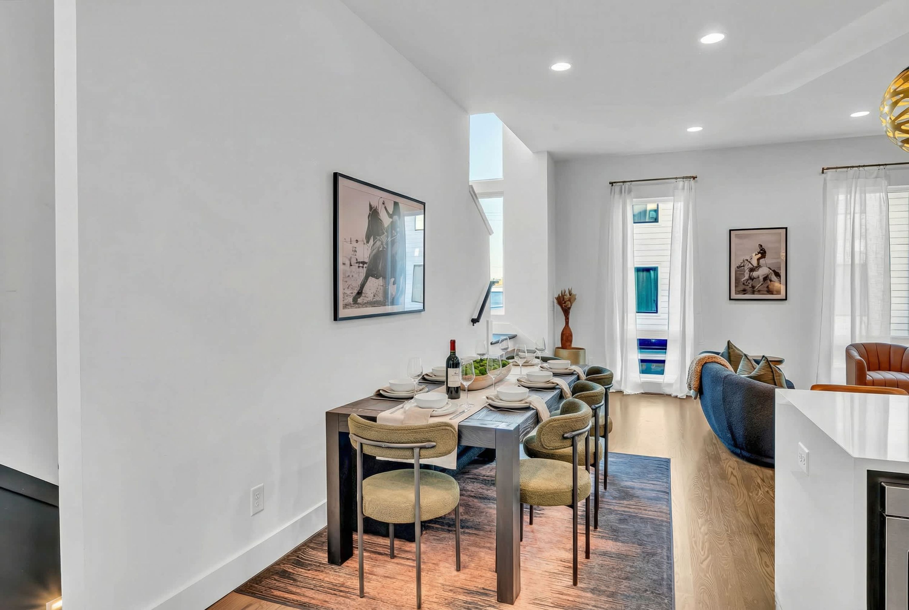 A modern dining area with a long table set for six, a sofa, and a kitchen area visible to the right.