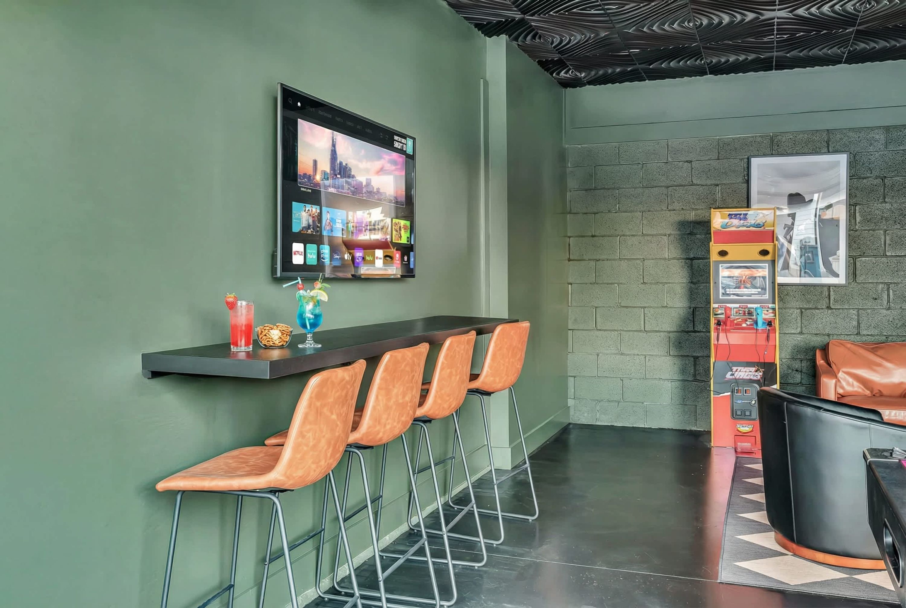 A bar area with a digital screen, bar stools, a vending machine, and a seating area.