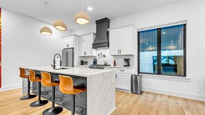 A modern kitchen with a marble island, bar stools, and a large window. - Two Homes Hot Tub Rooftop Deck in Nashville (Nashville)
