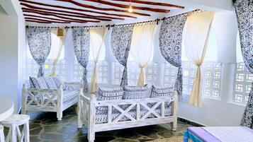A room with two wooden beds, patterned curtains, and a stone-tiled floor.