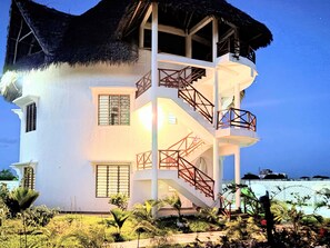 A multi-story building with a thatched roof, a balcony, and a staircase.