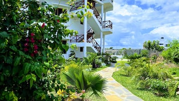 A white building with a thatched roof, a stone pathway, and lush greenery.