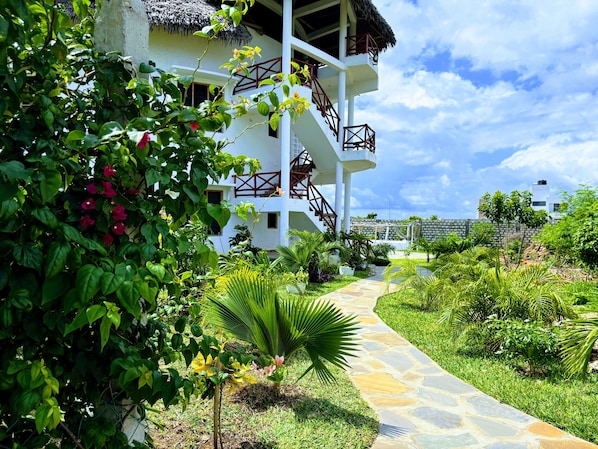 A white building with a thatched roof, a stone pathway, and lush greenery.
