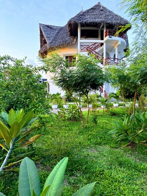 A building with a thatched roof, surrounded by lush greenery and a well-maintained garden.