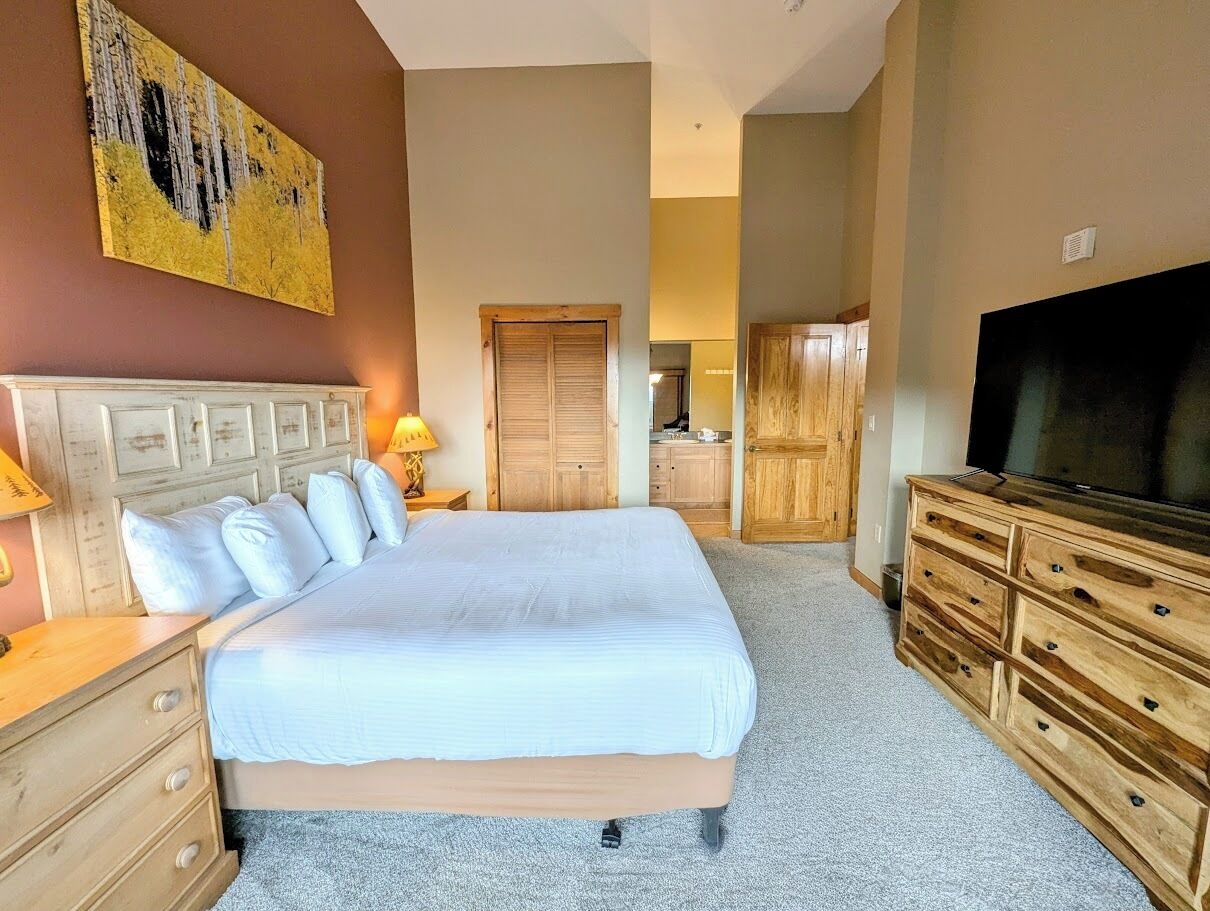 A hotel room with a large bed, wooden dresser, TV, and a painting on the wall.