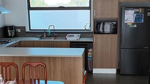 A modern kitchen with wooden cabinets, a built-in oven, and a refrigerator. There is a dining table with chairs and a window above the sink.