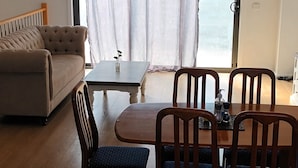 A modern living room with a sofa, dining table, chairs, and a view of the sea through large windows.