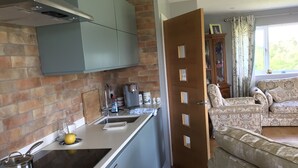 A kitchen with a modern design, a dining area with patterned furniture, and a view of the outdoors through a window. - More Than Just a Room Apartment Carlisle / Borders (Carlisle)