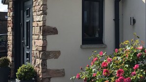 A stone building with a black door and window, surrounded by pink roses. - More Than Just a Room Apartment Carlisle / Borders (Carlisle)