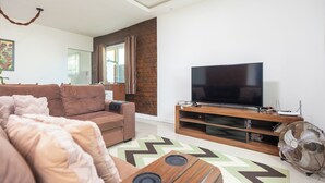 Uma sala de estar moderna com um sofá marrom, uma televisão de tela plana em um suporte de madeira e um ventilador.