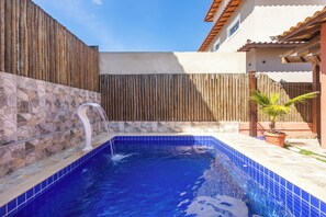 Una piscina con cascada, rodeada por una cerca de madera y un muro de piedra.