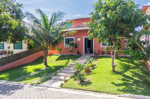Una casa con fachada roja, techo de tejas y un jardín bien cuidado con palmeras y un camino de piedra que lleva a la entrada.