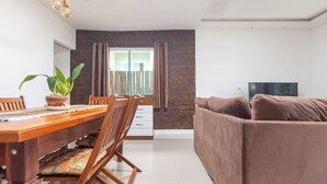 Uma sala de estar moderna com um sofá marrom, uma mesa de jantar de madeira com cadeiras, uma planta em vaso e uma televisão de tela plana.