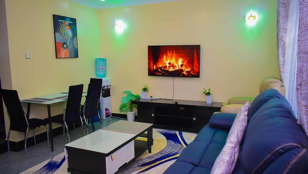 Een woonkamer met een bank, een salontafel, een aan de muur bevestigde televisie en een open haard.