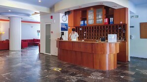 Aula, jossa on puinen vastaanottotiski, seinäkello ja punaisilla sohvilla varustettu oleskelualue.