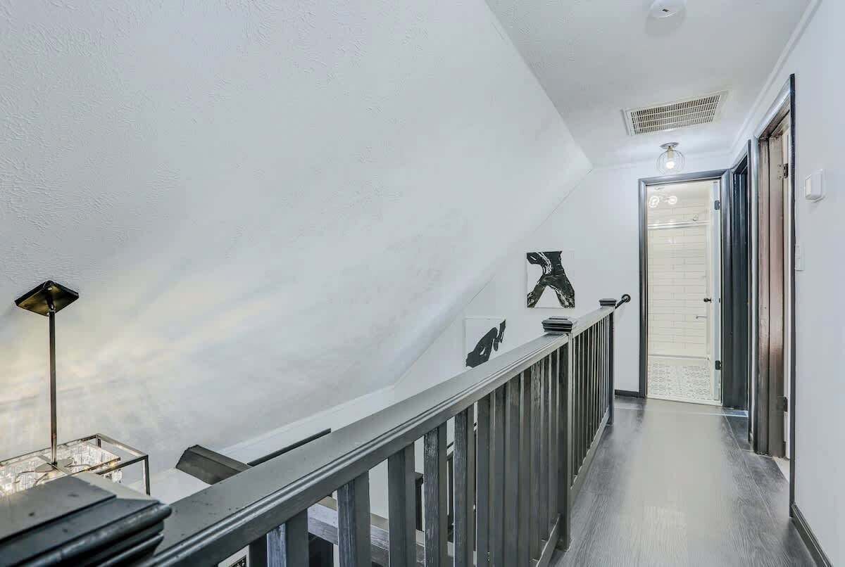 Un escalier moderne avec une rampe en verre, une bouche d’aération au plafond et une porte donnant sur un garage.